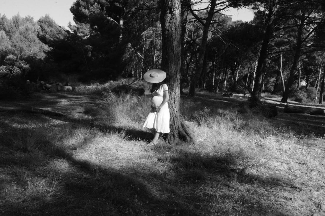 Future maman adossée à un pin en forêt, ventre rond en contre-jour, séance maternité fine art